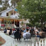 Audience practicing good house show etiquette seated in a front yard watching a band play on the porch in Davis