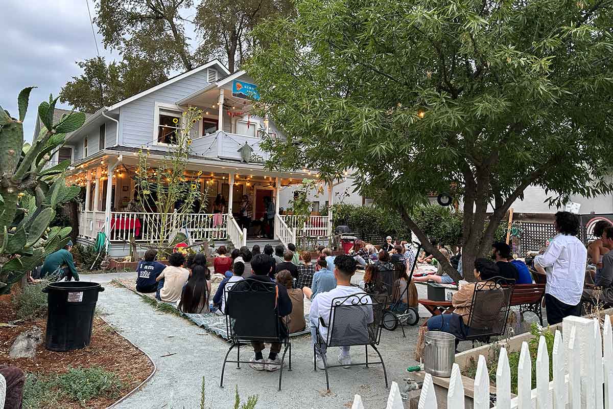 Audience practicing good house show etiquette seated in a front yard watching a band play on the porch in Davis